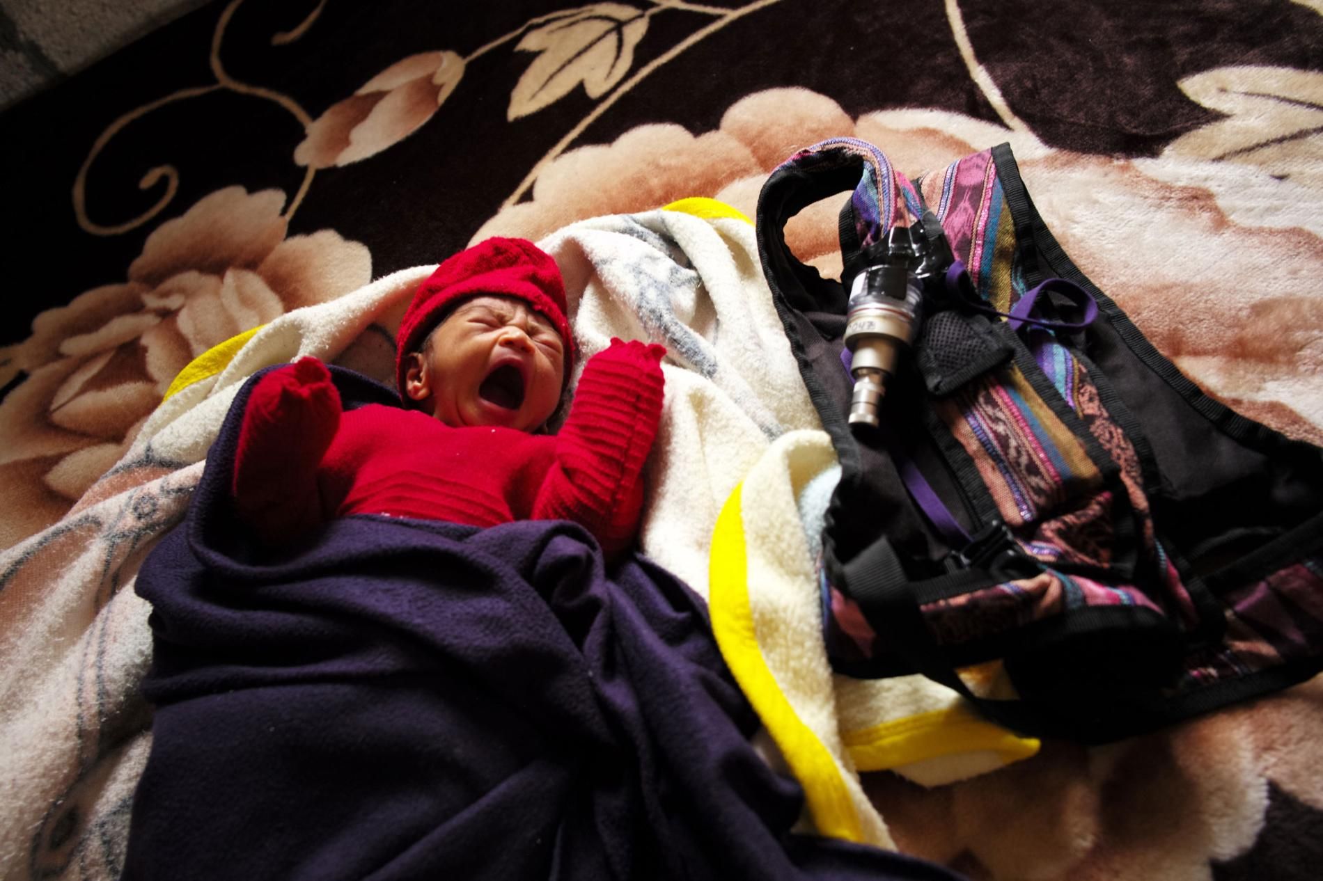 Dina Marroquín’s eight-day-old baby rests next to a knapsack holding an indoor air monitor—part of study being done by an international research team to determine whether the use of gas stoves improves air quality and the health of children. Image by Lynn Johnson. Guatemala, 2017.