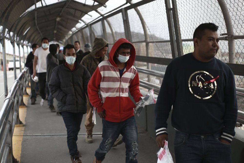 In this March 21, 2020 file photo, Central American migrants seeking asylum, some wearing protective face masks, return to Mexico via the international bridge at the U.S-Mexico border that joins Ciudad Juarez and El Paso. (AP Photo/Christian Chavez)