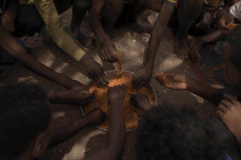 Ethiopian migrants eat spaghetti as they take shelter under a tree, in Obock, Djibouti. Image by AP Photo/Nariman El-Mofty. Djibouti, 2020.