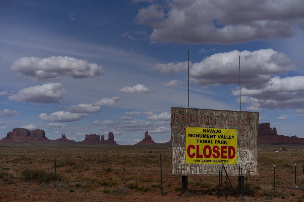 A sign reads "Navajo Monument Vally Tribal Park Closed Until Further Notice" posted at the entrance of Monument Valley in Oljato-Monument Valley, Utah, on the Navajo reservation April 19, 2020. The reservation has some of the highest rates of coronavirus in the country. If Navajos are susceptible to the virus' spread in part because they are so closely knit, that's also how many believe they will beat it. Image by AP Photo/Carolyn Kaster. United States, 2020.