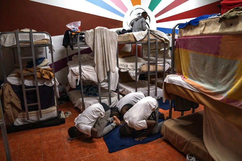 Asylum-seekers pray next to their beds at the Modern Christian Mission Church in Fuerteventura, one of the Canary Islands, Spain, on Saturday, Aug. 22, 2020. Image by Emilio Morenatti/AP Photo. Spain, 2020.