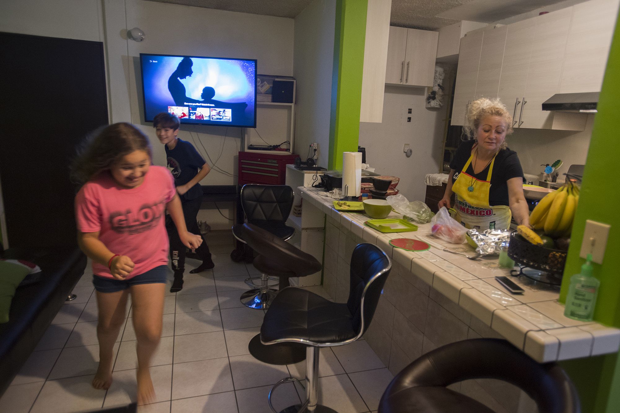 Rayma Flores, from left, and Edward get restless before dinner as their mother, Enedis, prepares the Thanksgiving feast on Nov. 28. When they are in Tijuana, the kids spend most of their time in the two-bedroom, one-bath apartment. Image by Amanda Cowan. Mexico, 2019.