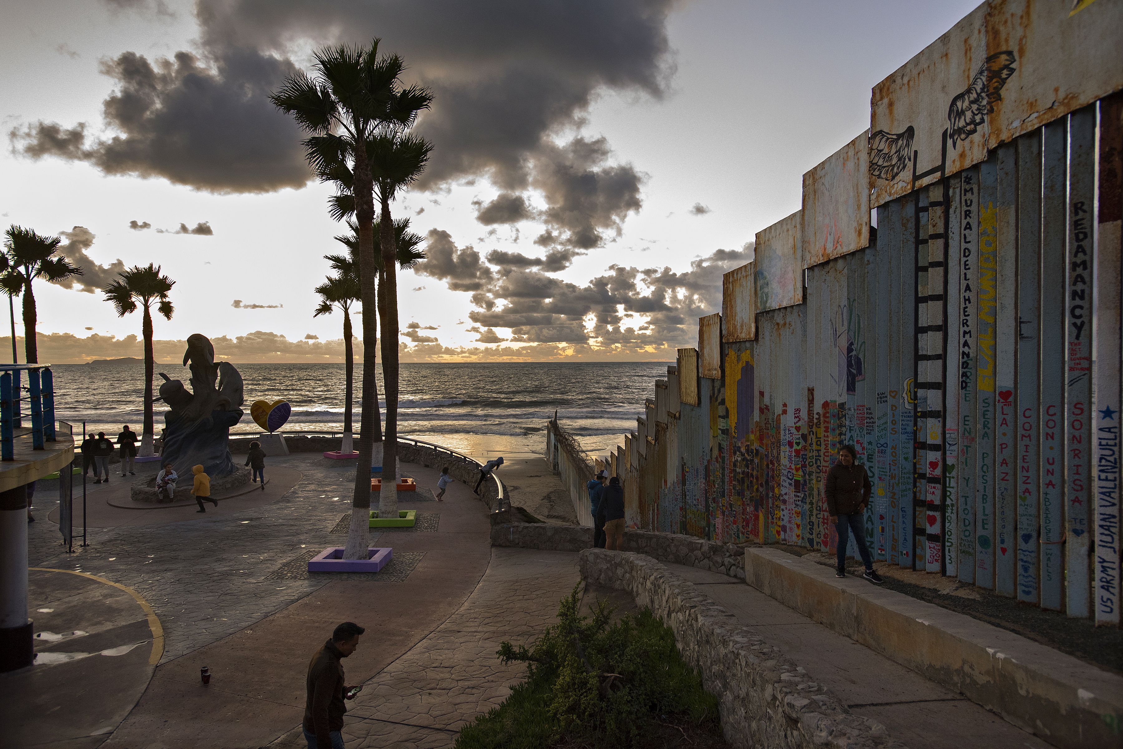 Visitors to Playas de Tijuana stop by the border wall at Friendship Park after sunset Nov. 29. The artwork along the border wall is temporary and changes frequently. Image by Amanda Cowan. Mexico, 2019.