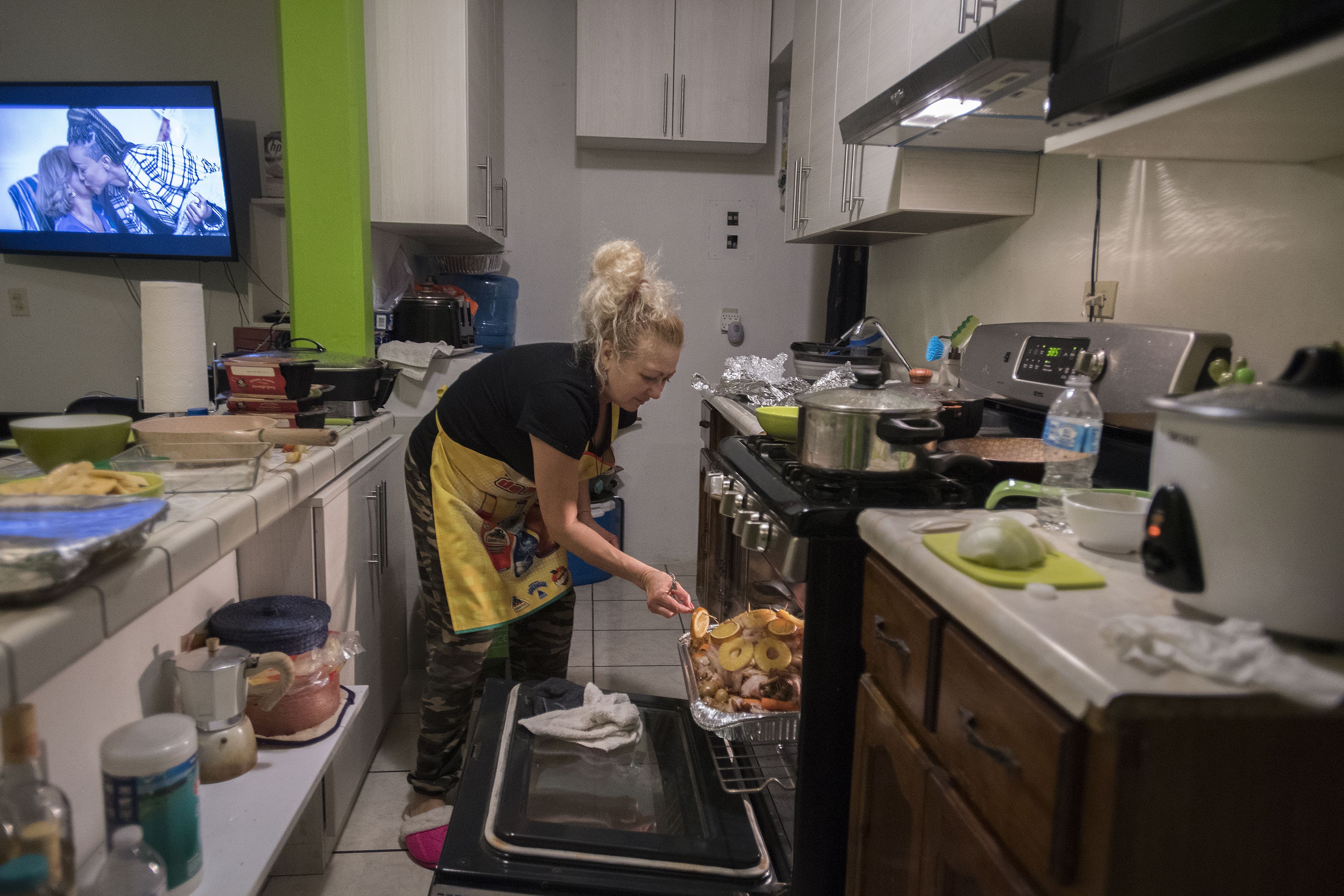 Enedis Flores takes a minute to check on the turkey, which is cooked with bacon, pineapple and oranges, while making Thanksgiving dinner for her family in her husband’s Tijuana apartment. Image by Amanda Cowan. Mexico, 2019.