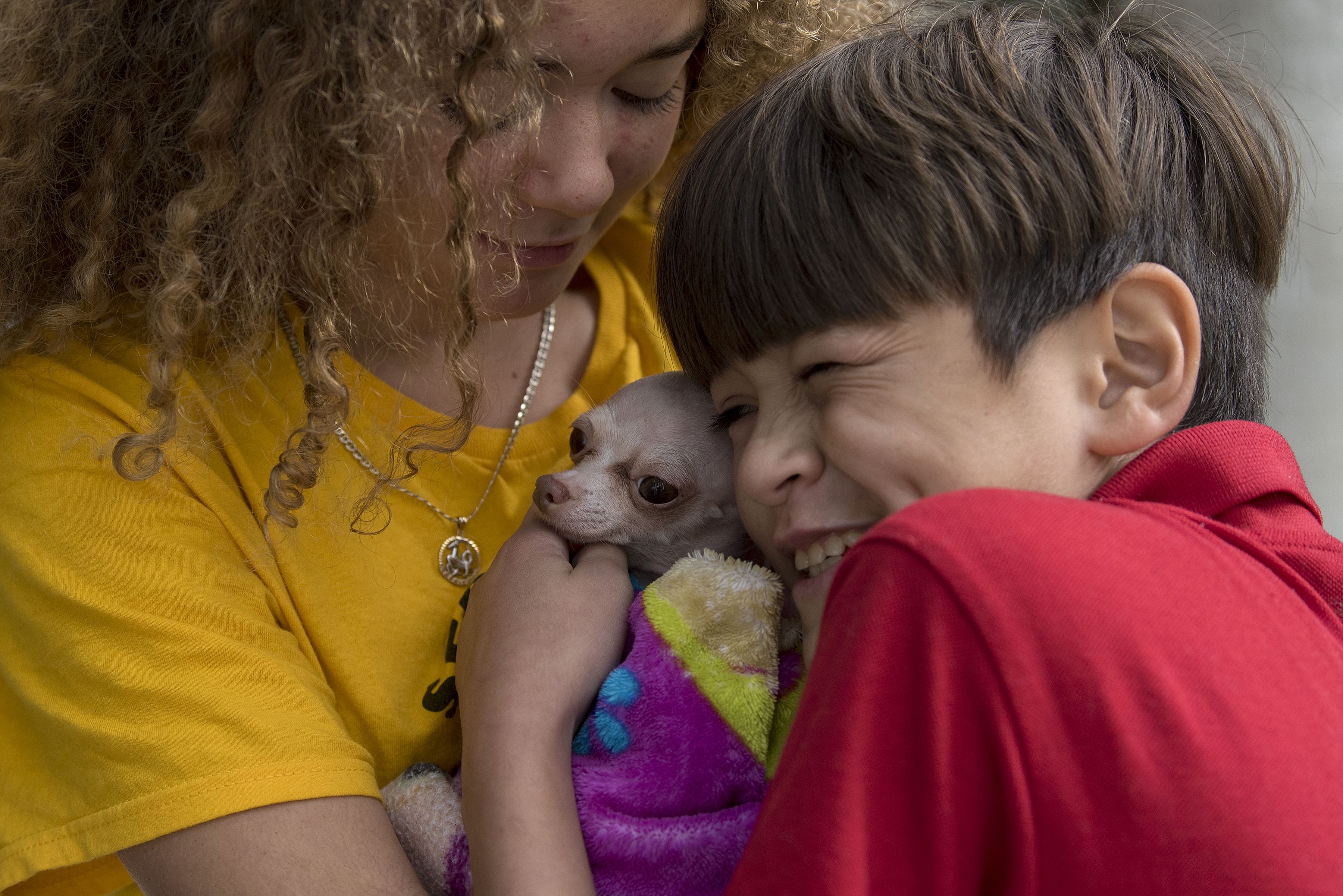 Kennedy Flores and her brother, Edward, cuddle with family dog, Bambi, as they visit their father for the Thanksgiving holiday in Tijuana, Mexico. Image by Amanda Cowan. Mexico, 2019.