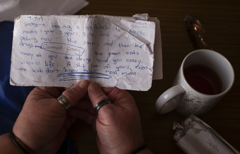 Carmall Casey reads a note she wrote while sitting at her home in Black River, Tasmania, Australia, Wednesday, July 24, 2019. One day, she scrawled her anguish on a tattered envelope. "Imagine having a toothache for weeks, months 1 year, 2 years, 3, 4, and it's still aching now ... the pain eats away at you, the drugs send you crazy," she wrote. "Even the kids don't know their real mum." Image by David Goldman. Australia, 2019.