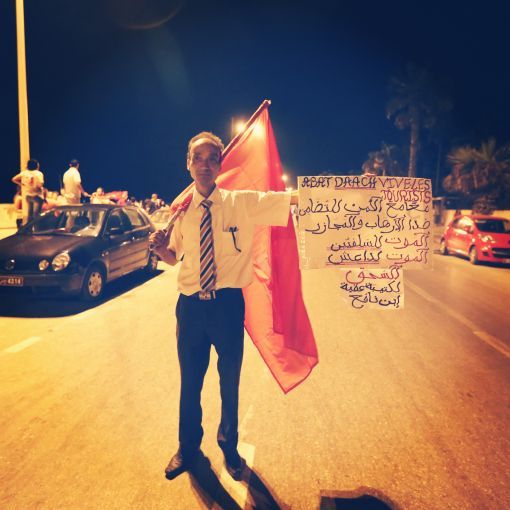 At a protest the evening following a mass beach shooting attack, a Tunisian man in Sousse holds up a banner in French and Arabic condemning ISIL and showing solidarity with the foreign tourists who were targeted. Image by Alice Su. Tunisia, 2015.