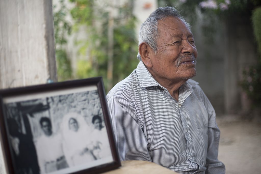 Humberto Contreras Zuñiga, Winny Contreras's father, sits in his home in Mexico next to a photo from his wedding day. Image by Ingrid Holmquist. Mexico, 2018.