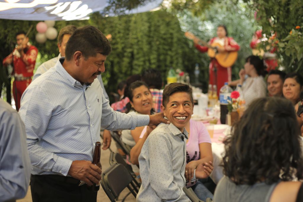 Winny Contreras laughs with his son Ricardo as a mariachi band plays at his eldest daughter's graduation party in their home in Mexico. Image by Ingrid Holmquist. Mexico, 2018.