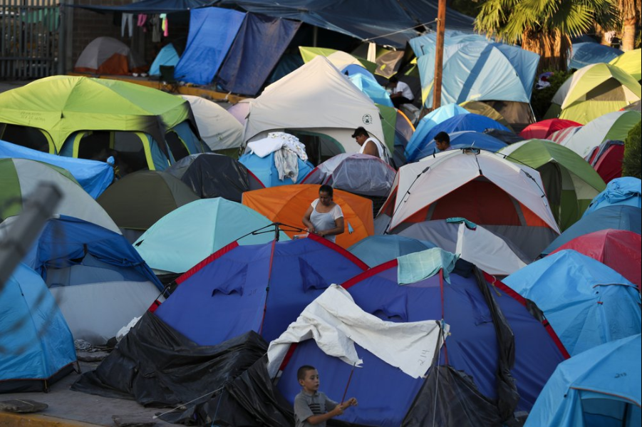 In this Oct. 11, 2019 photo, migrants wake up at a camp set up by migrants waiting near a legal port of entry bridge in Matamoros, Mexico. In years past, migrants seeking asylum in the United States moved quickly through this violent territory on their way to the U.S., but now due to Trump administration policies, they remain here for weeks and sometimes months as they await their U.S. court dates, often in the hands of gangsters who hold Tamaulipas state in a vice-like grip. Image by Fernando Llano. Mexico, 2019.