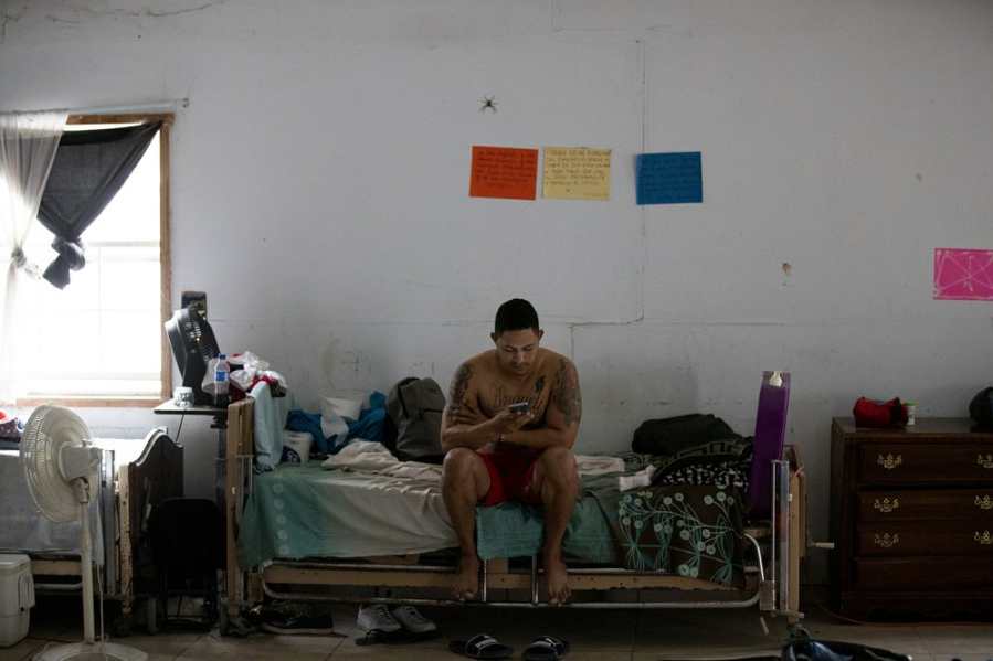 In this Oct. 12, 2019 photo, a Cuban migrant checks his cell phone at a migrant shelter in Reynosa, Mexico, Saturday, Oct. 12, 2019. In years past, migrants seeking asylum in the United States moved quickly through this violent territory on their way to the U.S., but now due to Trump administration policies, they remain here for weeks and sometimes months as they await their U.S. court dates, often in the hands of gangsters who hold Tamaulipas state in a vice-like grip. Image by Fernando Llano. Mexico, 2019.
