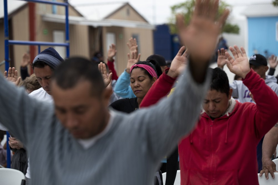 In this Oct. 12, 2019 photo, Cubans pray at a migrant shelter in Reynosa, Mexico. In years past, migrants seeking asylum in the United States moved quickly through this violent territory on their way to the U.S., but now due to Trump administration policies, they remain here for weeks and sometimes months as they await their U.S. court dates, often in the hands of gangsters who hold Tamaulipas state in a vice-like grip. Image by Fernando Llano. Mexico, 2019.