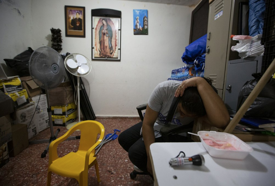 In this Sept. 18, 2019 photo, the wife of Nicaraguan migrant Yohan leans over a cell phone to speak with her family in Nicaragua, a she sits in the kitchen of a migrant shelter where she lives with her husband and son in Monterrey, Mexico. Linda's family left Nicaragua after armed, government-aligned civilian militias learned that Yohan had witnessed the killing of a government opponent, he said. They followed him and painted death threats on the walls of their home. Image by Fernando Llano. Mexico, 2019.