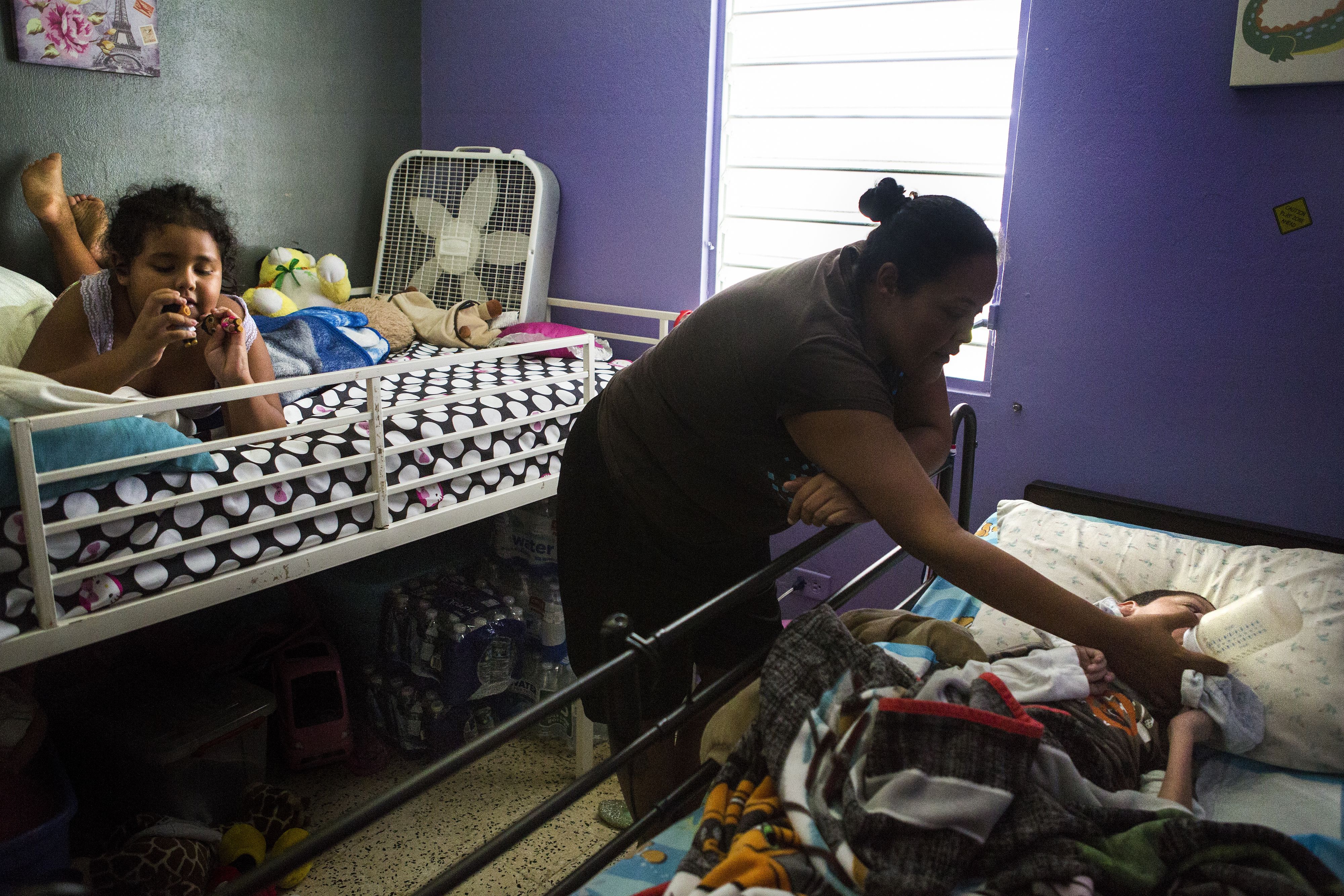 Karen Feliciano, center, feeds her oldest child, Kenny, 18, who suffers from a number of neurological and physical conditions, while her youngest daughter Kylia, who suffers from autism plays on the bed in their home. “When [Kenny] was born, the doctors said he would only live to six,” Karen said. Image by Ryan Michalesko. Puerto Rico, 2017.