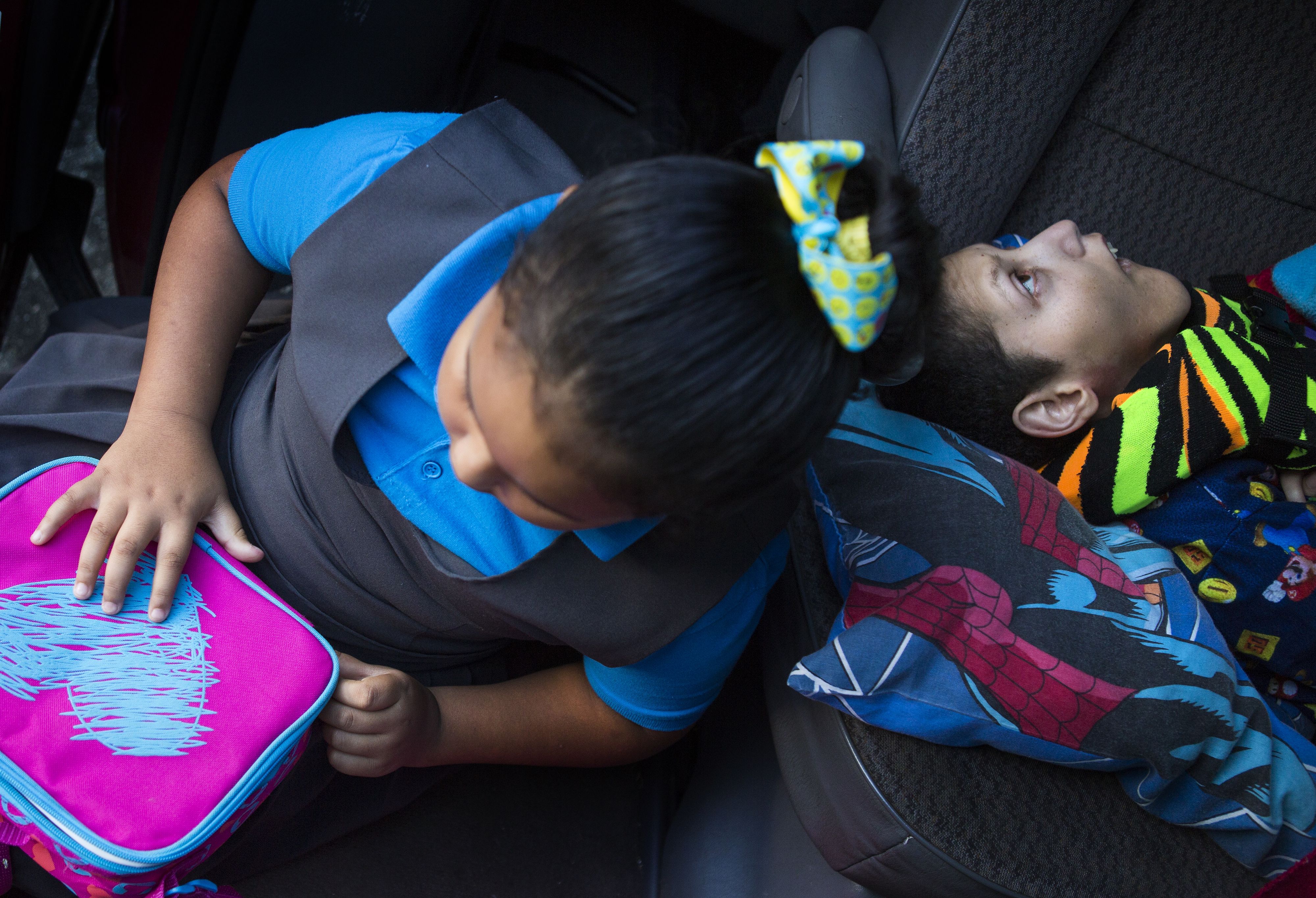 Kylia Jimenez Feliciano, 6, left, who suffers from autism, zips her lunch box as her brother Kenny, lies across the bench seat of the family van prior to leaving for school. Image by Ryan Michalesko. Puerto Rico, 2017.