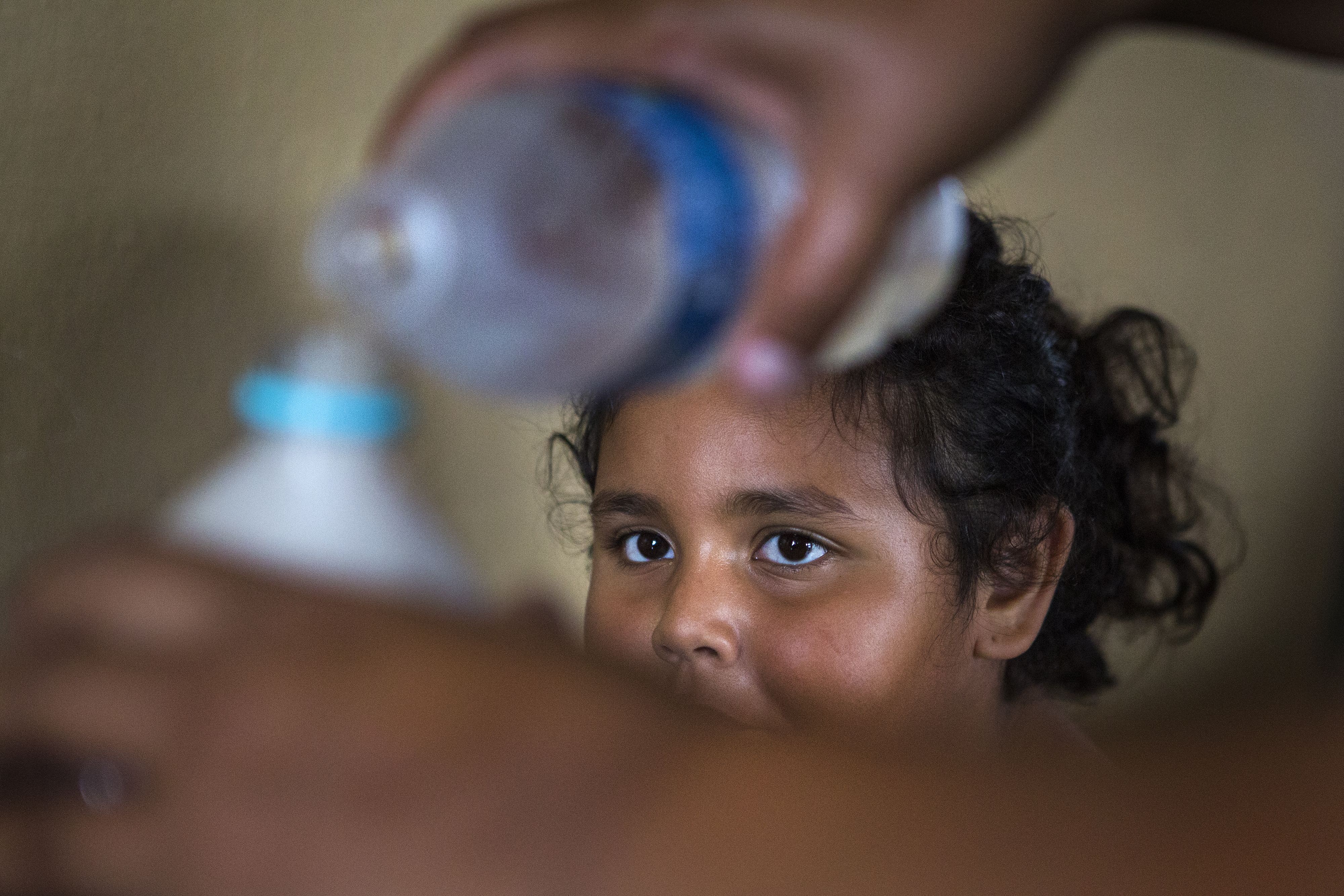 Kylia Jimenez Feliciano watches as her mother, Karen, fills a bottle with drinking water in the kitchen of the family's Aibonito home. Image by Ryan Michalesko. Puerto Rico, 2017.