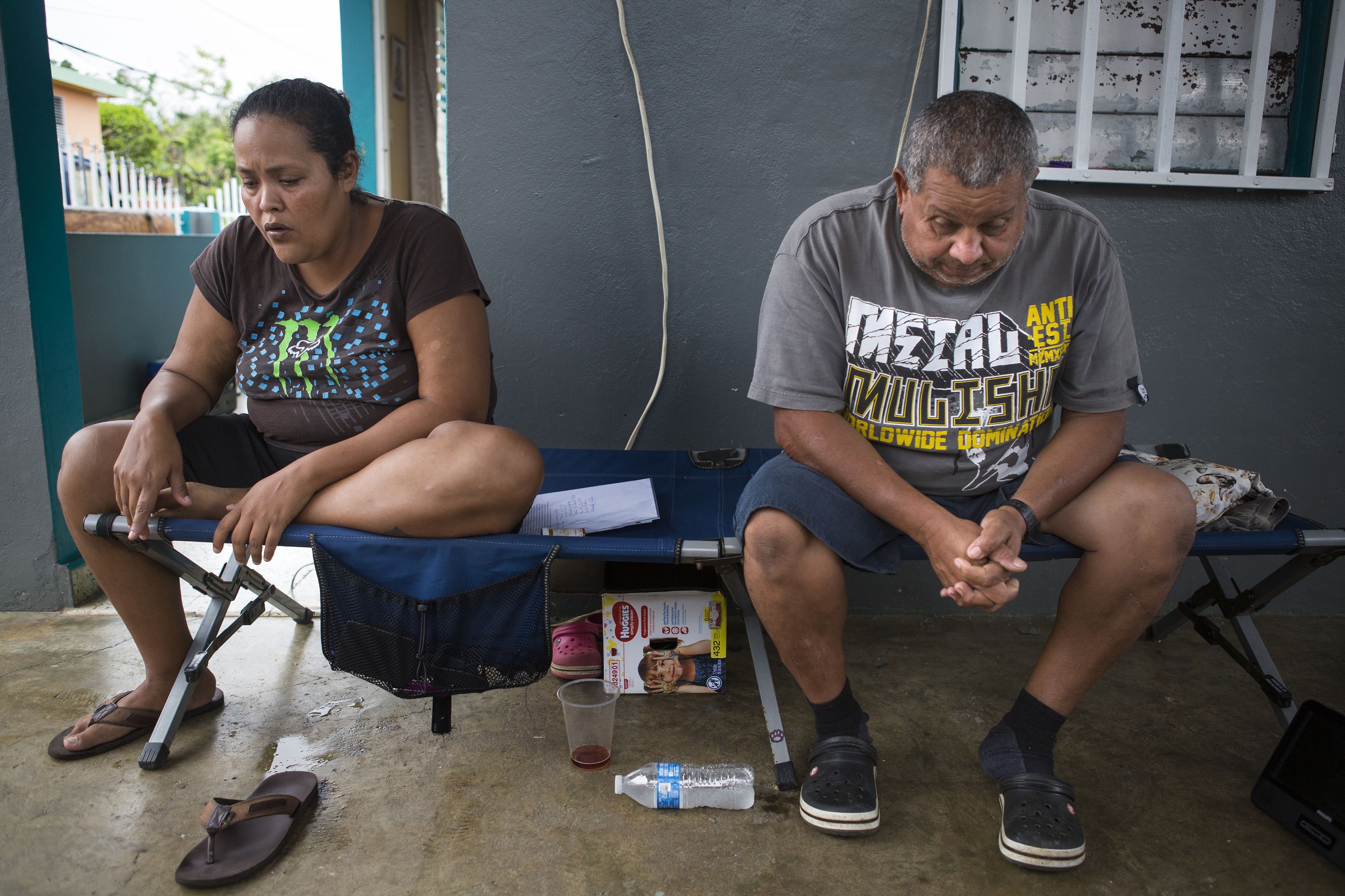 Karen Feliciano, left, and her husband take time to themselves while seated on a folding cot set up on their porch. Image by Ryan Michalesko. Puerto Rico, 2017.