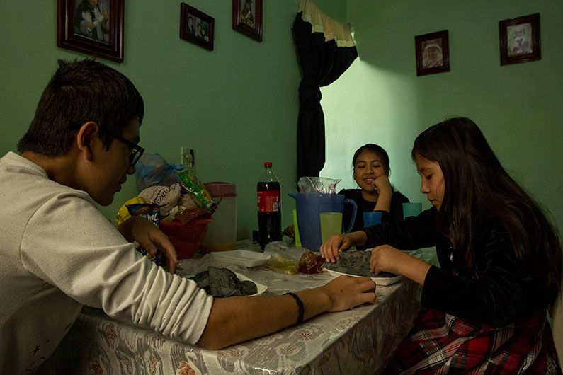 Siblings Jared, 14, Ayleen, 11, and Paulina eat lunch together. The Zarazua children have scholarships from the Mexican government to attend school and special classes. Image by Erika Schultz. Mexico, 2019.