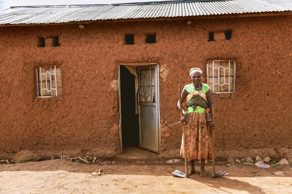 A Rwandan woman stands in front of her home. Image by sifkigali/Shutterstock. Rwanda, 2015.