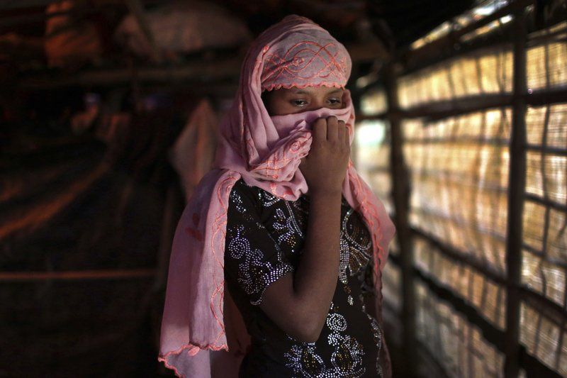 In this Sunday, Nov. 19, 2017, photo, R, 13, covers her face with her headscarf while being photographed in her tent in Kutupalong refugee camp in Bangladesh. The Associated Press has found that the rape of Rohingya women by Myanmar’s security forces has been sweeping and methodical. The AP interviewed 29 women and girls who say they were raped by Myanmar’s armed forces, and found distinct patterns in their accounts, their assailants’ uniforms and the details of the rapes themselves. The most common attack involved groups of soldiers storming into a house, beating any children inside and then beating and gang raping the women. Image by Wong Maye-E. Bangladesh, 2017.