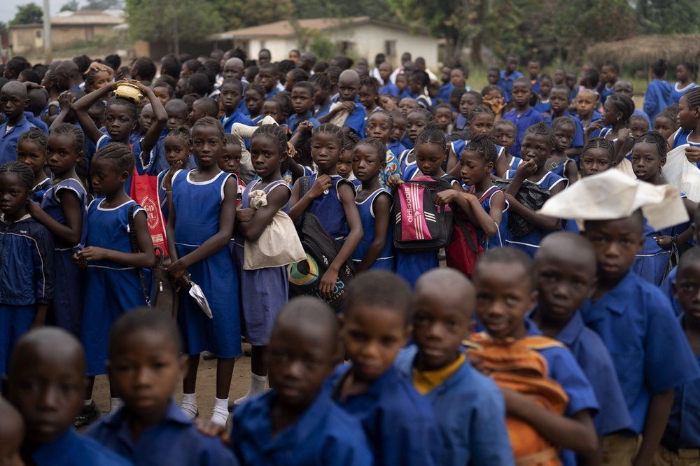 Primary students gather in line before they enter their classrooms at Kombayendeh village in Lei chiefdom, district of Kono, Sierra Leone, Friday, Nov. 27, 2020. Early marriages were happening so often in this part of Sierra Leone that traditional leaders in the Lei chiefdom instituted a new bylaw imposing a 500,000 ($50) fine on anyone having sex with a minor, even if the man is married to the child. Yet local leaders in Kombayendeh can't recall a single fine being issued. Image by Leo Correa/AP Photo. Sierra Leone, 2020.

