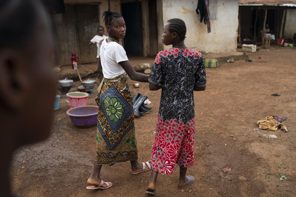 Marie walks with a friend on a street in Komao village, on the outskirts of Koidu, district of Kono, Sierra Leone, Sunday, Nov. 22, 2020. A man, in his mid-20s, first caught a glimpse of Marie as she ran with her friends past his house near the village primary school. Soon after, he proposed to the fifth-grader. “I’m going to school now. I don’t want to get married and stay in the house,” she told him. But the pressures of a global pandemic on this remote corner of Sierra Leone were greater than the wishes of a schoolgirl. Image by Leo Correa/AP Photo. Sierra Leone, 2020.