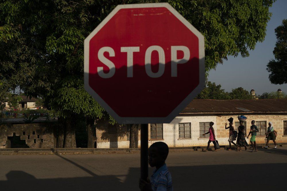 A boy walks past a stop sign in Koidu, district of Kono, Sierra Leone, Monday, Nov. 23, 2020. Only 76 coronavirus cases were confirmed in Kono district, but the economic toll here has brought many families already living on the edge to a breaking point. Image by Leo Correa/AP Photo. Sierra Leone, 2020.