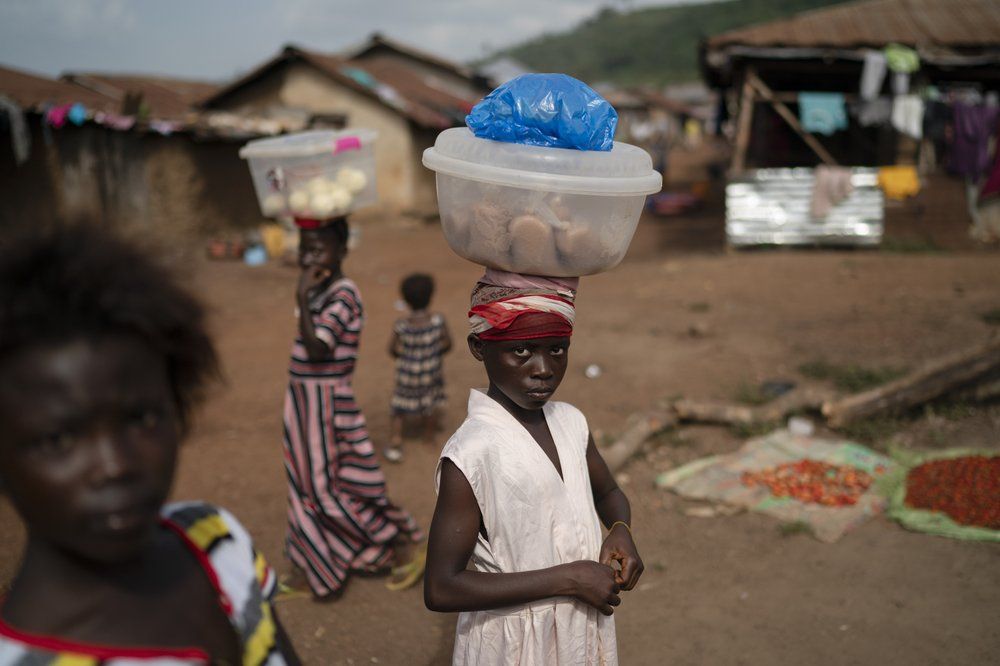 Isatu, 12, carries packets of rice flour to sell at Komao village, on the outskirts of Koidu, district of Kono, Sierra Leone, Sunday, Nov. 22, 2020. Sierra Leone closed its borders before the country had its first COVID-19 case. As a result, the country has seen only 2,434 confirmed cases and 74 deaths. Only 76 of those cases were confirmed in Kono district, but the economic toll here has brought many families already living on the edge to a breaking point. Image by Leo Correa/AP Photo. Sierra Leone, 2020.
