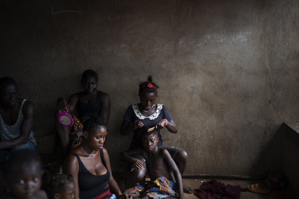 A woman combs the hair of a girl as they watch a video clip on a portable DVD player in Komao village, on the outskirts of Koidu, district of Kono, Sierra Leone, Sunday, Nov. 22, 2020. Image by Leo Correa/AP Photo. Sierra Leone, 2020.
