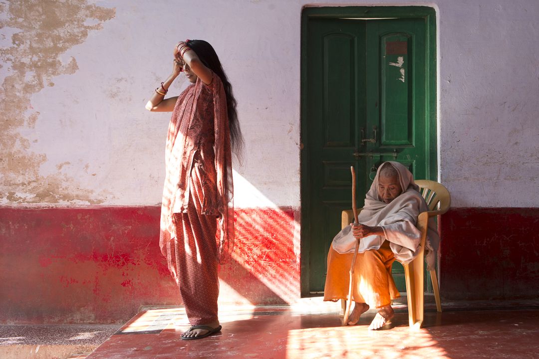 In a shelter in Vrindavan, known as a "city of widows," Lalita (at right) bears the cropped hair and white wrap of her culture once considered obligatory for widowhood. Shelter manager Ranjana, a much younger widow, is less constrained by traditional customs. Image by Amy Toensing. India, 2013.