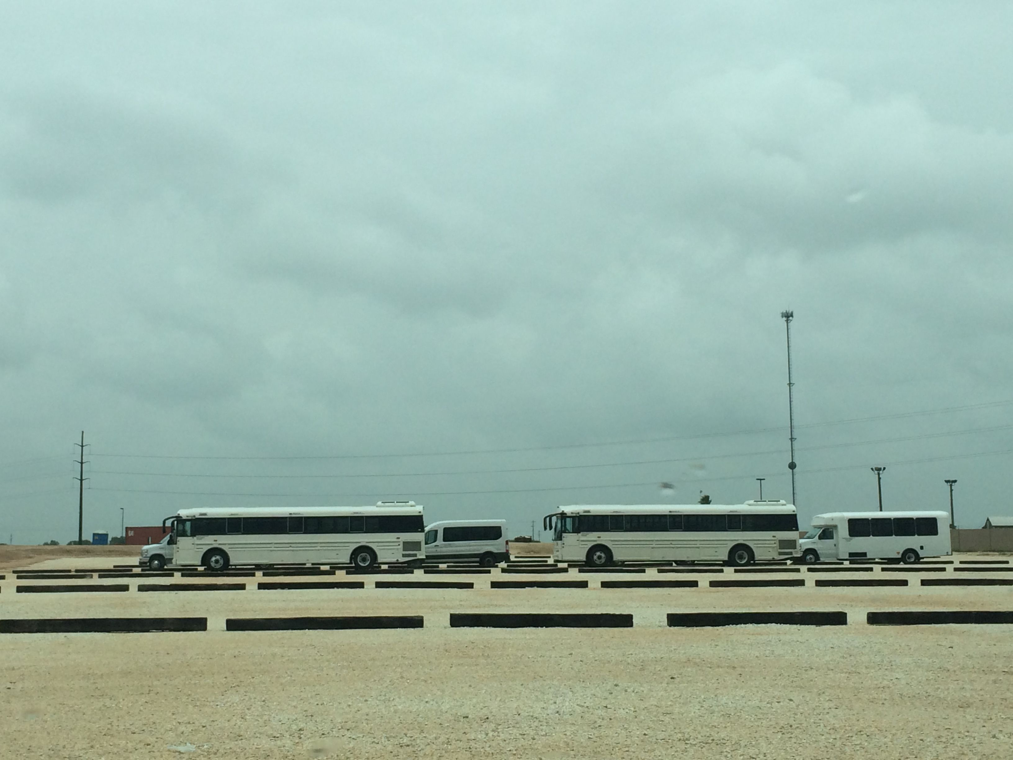 Buses used to transport asylum-seeking mothers and children wait outside a family detention center in Dilley, TX. Image by Emily Gogolak. United States, 2016.
