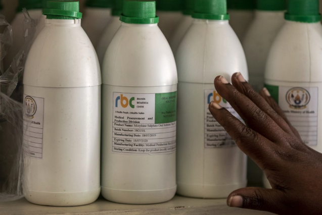 In this photo taken Monday, Nov. 4, 2019, a pharmacist shows bottles of locally-produced oral liquid morphine in the pharmacy of the district hospital in Kibogora, Rwanda. While people in rich countries are dying from overuse of prescription painkillers, people in Rwanda and other poor countries are suffering from a lack of them, but Rwanda has come up with a solution to its pain crisis - it's morphine, which costs just pennies to produce and is delivered to households across the country by public health workers. Image by Ben Curtis / AP Photo. Rwanda, 2019.
