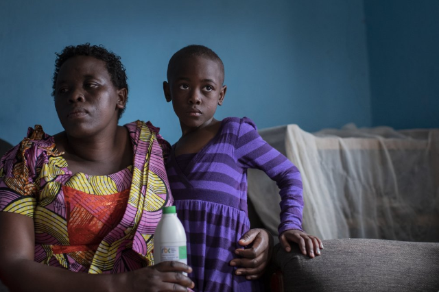 In this photo taken Wednesday, Nov. 6, 2019, mother Joselyne Mukanyabyenda, left, holds the bottle of oral liquid morphine that her daughter Ange Mucyo Izere, 6, right, uses to alleviate the pain of her bone marrow cancer, inside her home in the Gitega neighborhood of the capital Kigali, Rwanda. While people in rich countries are dying from overuse of prescription painkillers, people in Rwanda and other poor countries are suffering from a lack of them, but Rwanda has come up with a solution to its pain crisis - it's morphine, which costs just pennies to produce and is delivered to households across the country by public health workers. Image by Ben Curtis / AP Photo. Rwanda, 2019.