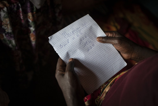 In this photo taken Monday, Nov. 4, 2019, Maria Mukamabano holds a handwritten note advising the schedule that her mother-in-law and cancer patient Athanasie Nyirangirababyeyi, 89, should take her oral liquid morphine for her pain, during a visit to check on her health by palliative care nurse Madeleine Mukantagara at her son's home in the village of Kagano, near Kibogora, in western Rwanda. While people in rich countries are dying from overuse of prescription painkillers, people in Rwanda and other poor countries are suffering from a lack of them, but Rwanda has come up with a solution to its pain crisis - it's morphine, which costs just pennies to produce and is delivered to households across the country by public health workers. Image by Ben Curtis / AP Photo. Rwanda, 2019.