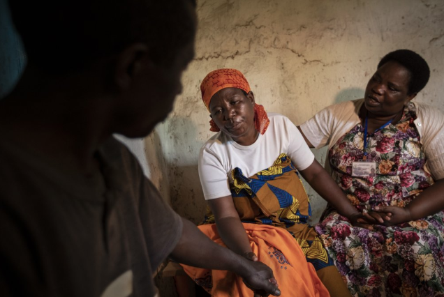In this photo taken Tuesday, Nov. 5, 2019, palliative care nurse Madeleine Mukantagara, 56, right, comforts and prays with Faina Nyirabaguiza, 52, center, who has cervical cancer, accompanied by Faina's husband Felicien Musemihari, left, after giving her an increased dose of oral liquid morphine during a visit to check on her health at her home in the village of Ruesero, near Kibogora, in western Rwanda. While people in rich countries are dying from overuse of prescription painkillers, people in Rwanda and other poor countries are suffering from a lack of them, but Rwanda has come up with a solution to its pain crisis - it's morphine, which costs just pennies to produce and is delivered to households across the country by public health workers. Image by Ben Curtis / AP Photo. Rwanda, 2019.