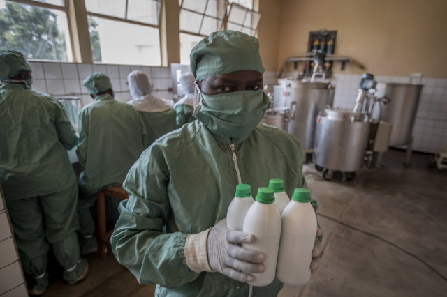 In this photo taken Thursday, Nov. 7, 2019, a worker carries bottles of liquid morphine after making it from powder, wearing protective clothing to protect from the effects of the drug and to prevent contamination, at the Pharmaceutical Laboratory of Rwanda in Butare, Rwanda. While people in rich countries are dying from overuse of prescription painkillers, people in Rwanda and other poor countries are suffering from a lack of them, but Rwanda has come up with a solution to its pain crisis - it's morphine, which costs just pennies to produce and is delivered to households across the country by public health workers. Image by Ben Curtis / AP Photo. Rwanda, 2019.