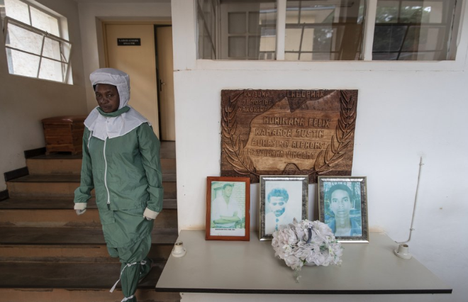 In this photo taken Thursday, Nov. 7, 2019, a worker who makes liquid morphine from powder wears protective clothing to protect from the effects of the drug and to prevent contamination, as she walks past a memorial to the four people working at the Pharmaceutical Laboratory of Rwanda who died in the country's 1994 genocide, at the facility in Butare, Rwanda. While people in rich countries are dying from overuse of prescription painkillers, people in Rwanda and other poor countries are suffering from a lack of them, but Rwanda has come up with a solution to its pain crisis - it's morphine, which costs just pennies to produce and is delivered to households across the country by public health workers. Image by Ben Curtis / AP Photo. Rwanda, 2019.