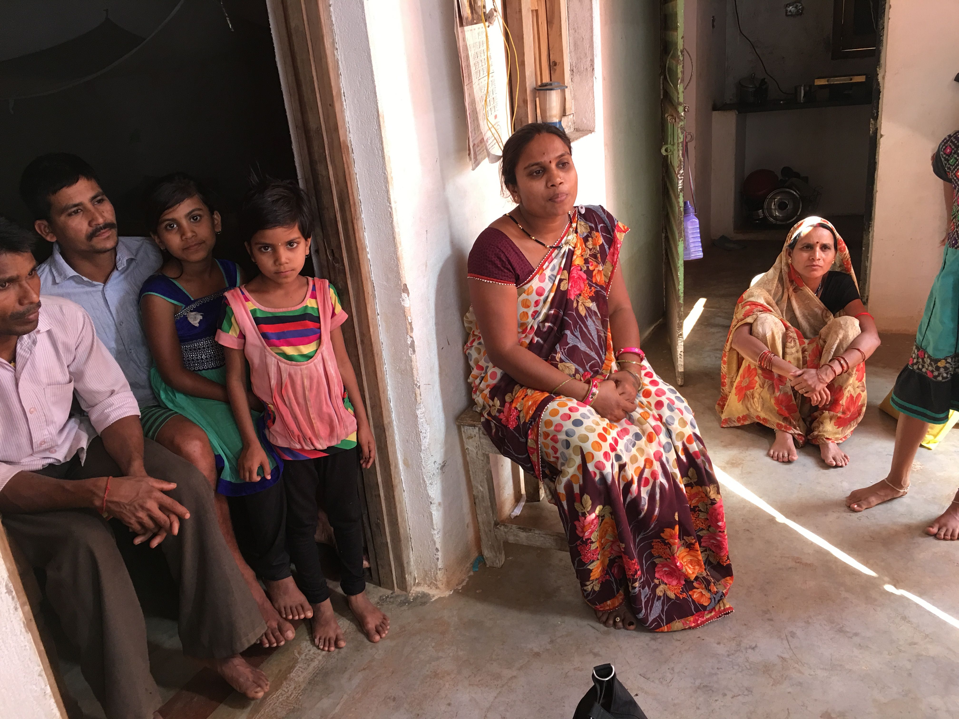 Pinki Sahu sits in a chair surrounded by family members. Pinki lost her sister, Sunita, when she died due to a botched sterilization procedure at a government-run camp in Chhattisgarh. Image by Hannah Harris Green. India, 2018.