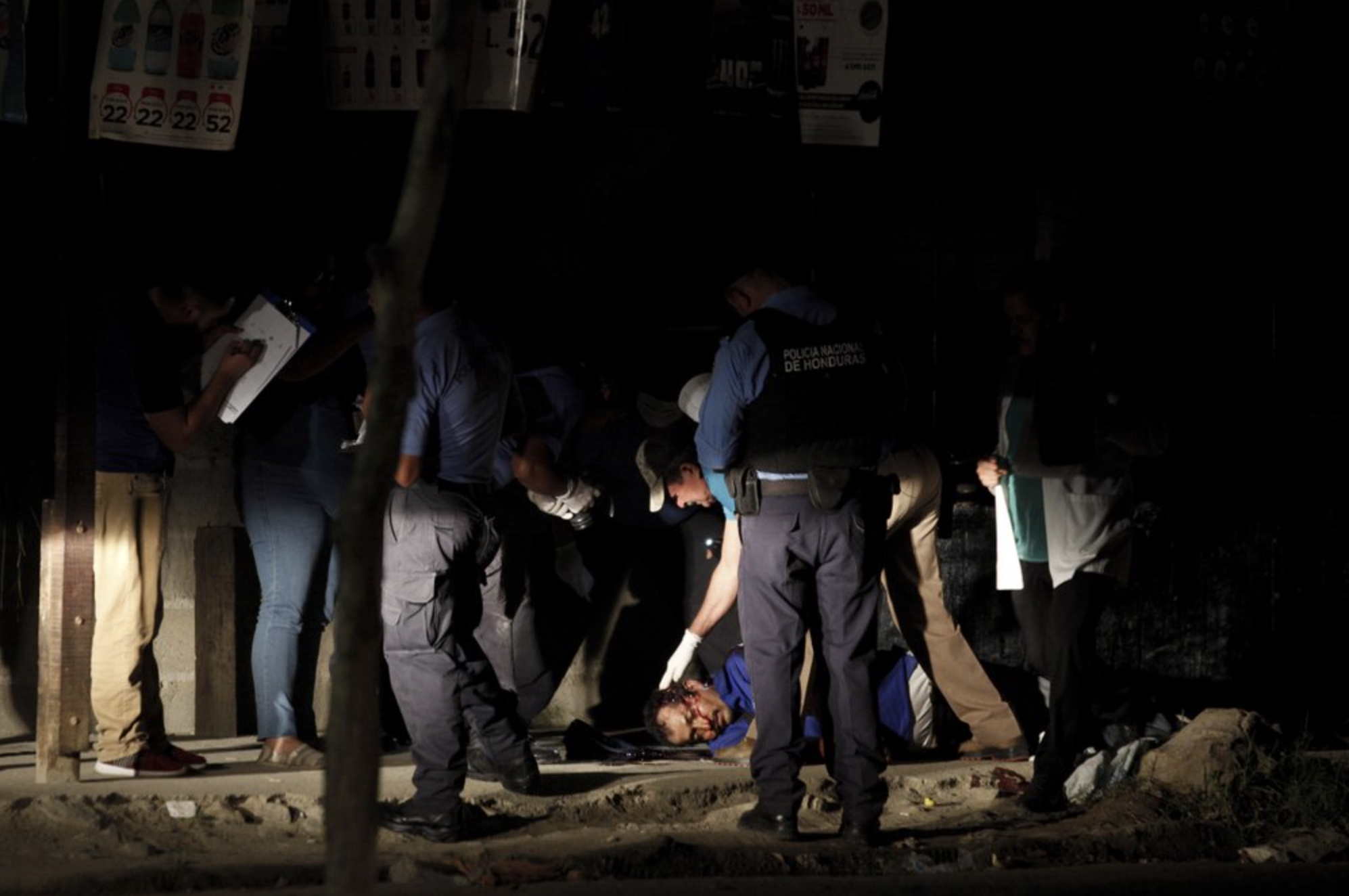 The body of a man lies in the middle of a street as police and forensic workers inspect the crime scene in the Rivera Hernandez neighborhood of San Pedro Sula, Honduras, on Nov. 30, 2019. Image by Moises Castillo/ AP Photo. Honduras, 2019.