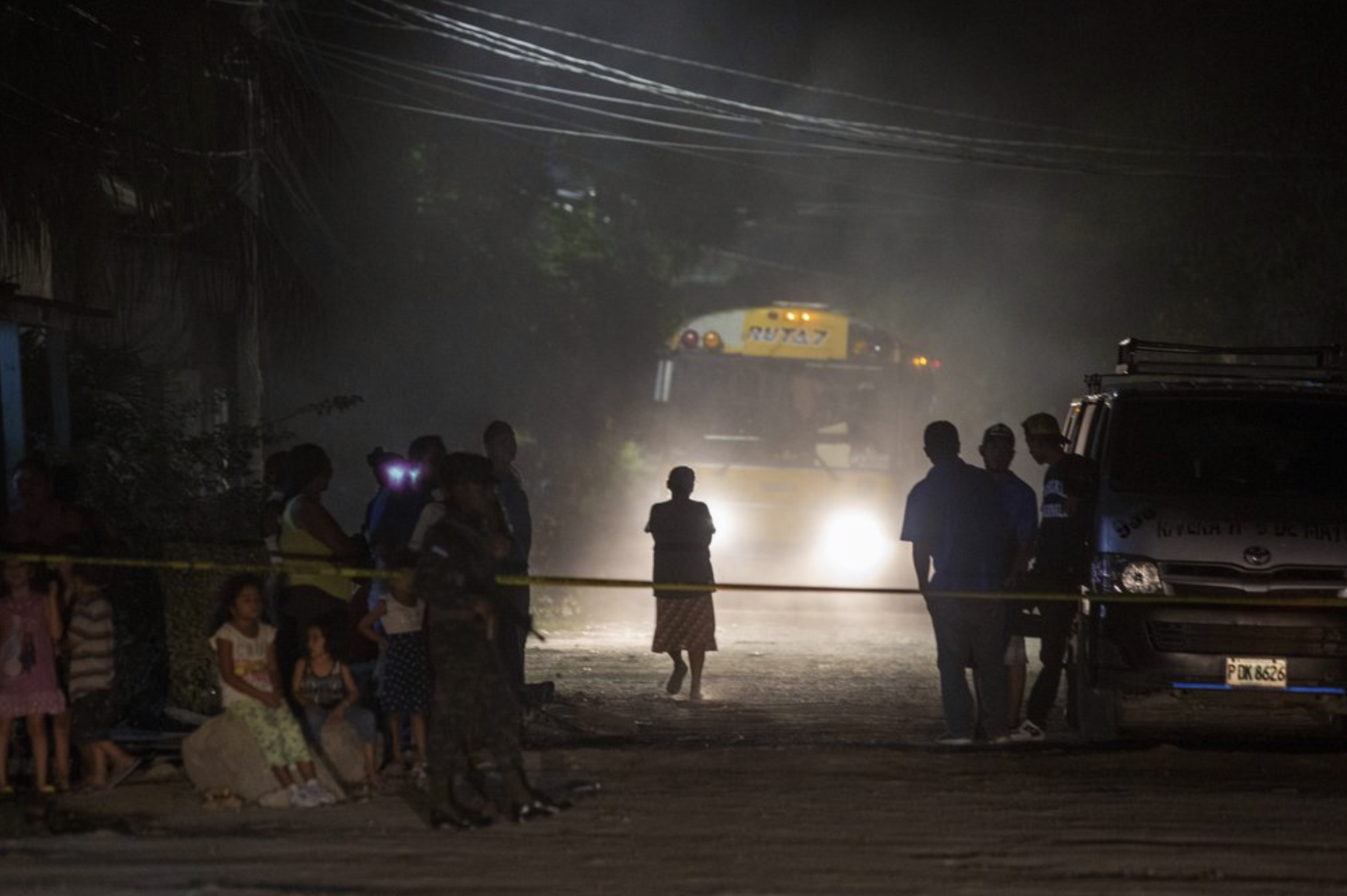 Neighbors watch as police and forensic workers inspect a body at a crime scene in the Rivera Hernandez neighborhood of San Pedro Sula, Honduras, on Nov. 30, 2019. Image by Moises Castillo/ AP Photo. Honduras, 2019.