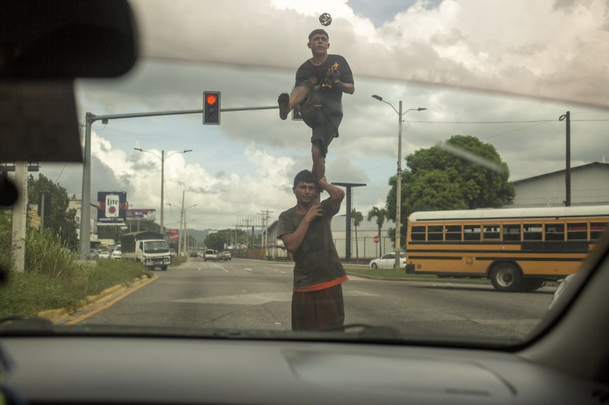 Two street jugglers perform on a corner for money in San Pedro Sula, Honduras on Nov. 28, 2019. The city's criminal life is dominated by two street gangs formed decades earlier in Latino enclaves of Los Angeles, spreading southward as gang members were deported. Today, MS-13 and Mara 18 are the most powerful and feared gangs in Central America, and have operations that reach from Mexico to the U.S. to Europe. Image by Moises Castillo/ AP Photo. Honduras, 2019.