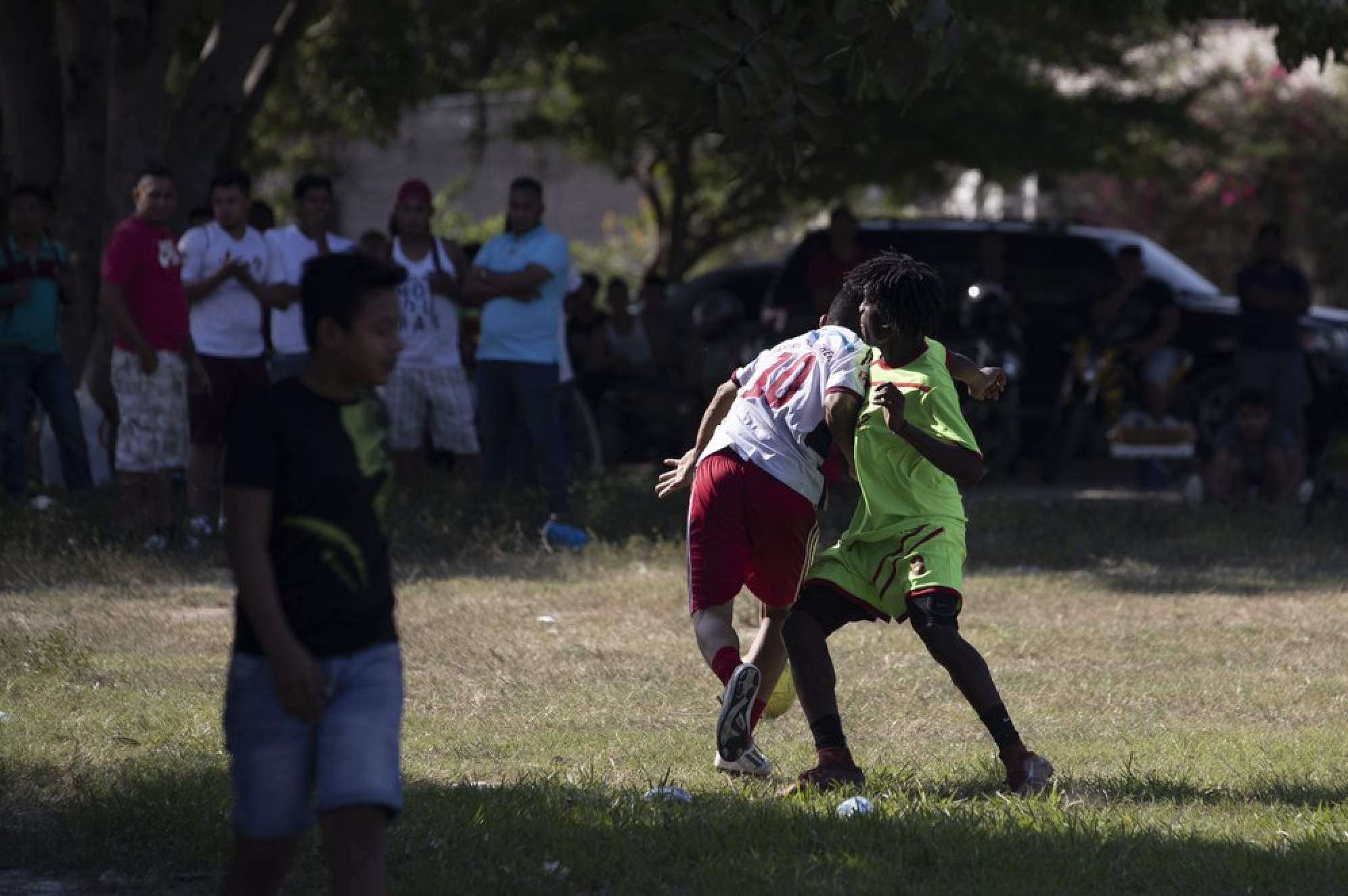 Players from a taxi drivers' team, center left, and a gang members' team vie for the soccer ball during a game in the Rivera Hernandez neighborhood of San Pedro Sula, Honduras, on Dec. 1, 2019. With the help of neighbors, an evangelical pastor organized a zone of tolerance in the field where 14 people were killed in 2010, during an inter-gang battle for control of the area. Image by Moises Castillo/ AP Photo. Honduras, 2019.