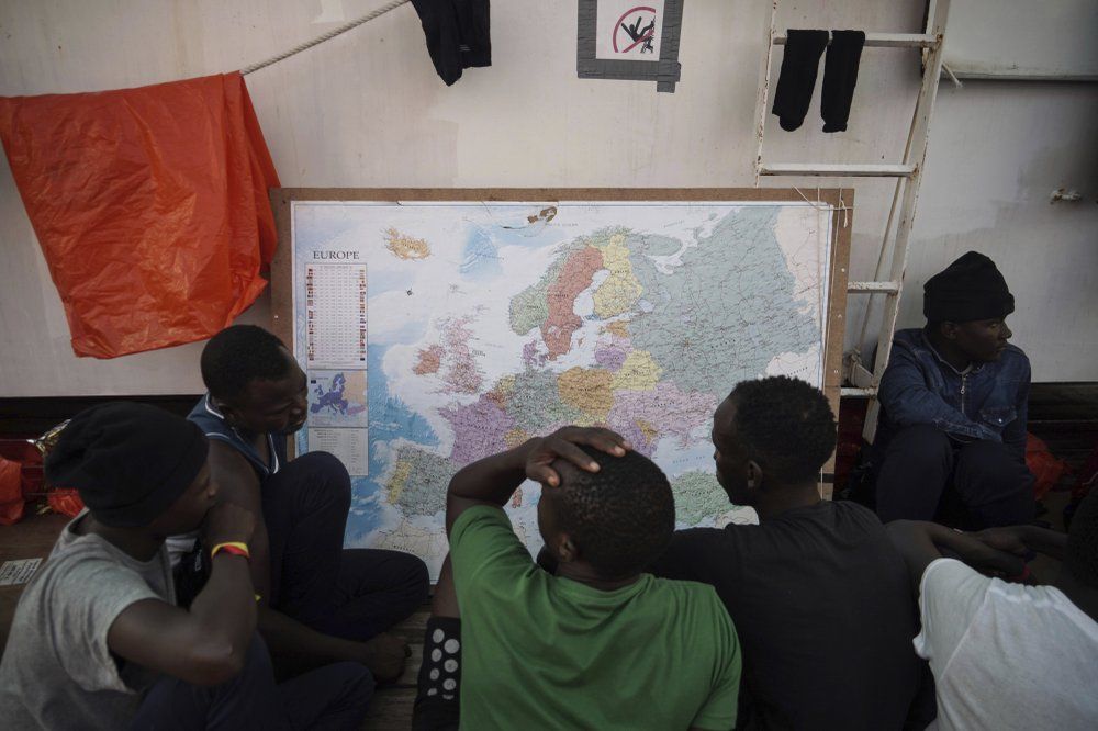 In this Sept. 23, 2019 photo, rescued migrants look at a map of Europe aboard the Ocean Viking humanitarian ship as it sails in the Mediterranean Sea. The misery of migrants in Libya has spawned a thriving and highly lucrative business, in part funded by the EU and enabled by the United Nations, an Associated Press investigation has found. Image by Renata Brito/AP Photo. Libya, 2019.
