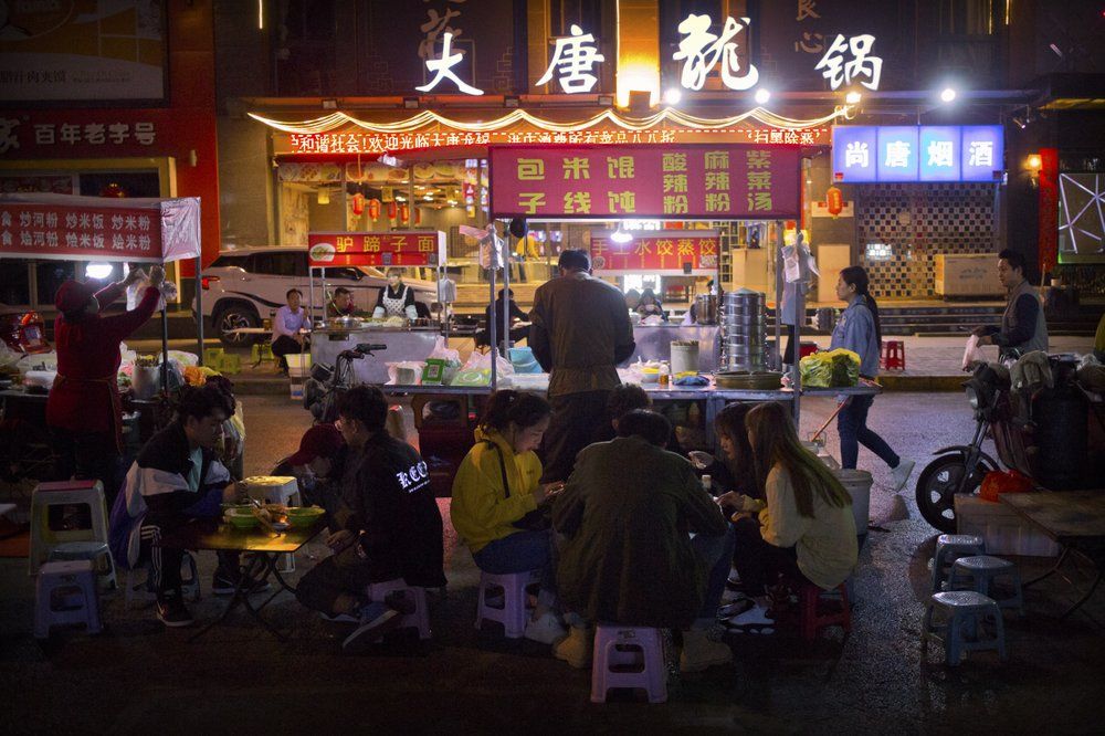 In this March 27, 2019, photo, people eat at an outdoor night market in Xi'an, northwestern China's Shaanxi Province, similar to one at which Yin Hao, who also goes by Yin Qiang, was injured during a fight that led to his initial prescription for Tylox. Officially, pain pill abuse is an American problem, not a Chinese one. But people in China have fallen into opioid abuse the same way many Americans did, through a doctor's prescription. And despite China's strict regulations, online trafficking networks, which facilitated the spread of opioids in the U.S., also exist in China. Image by Mark Schiefelbein/ AP Photo. China, 2019.