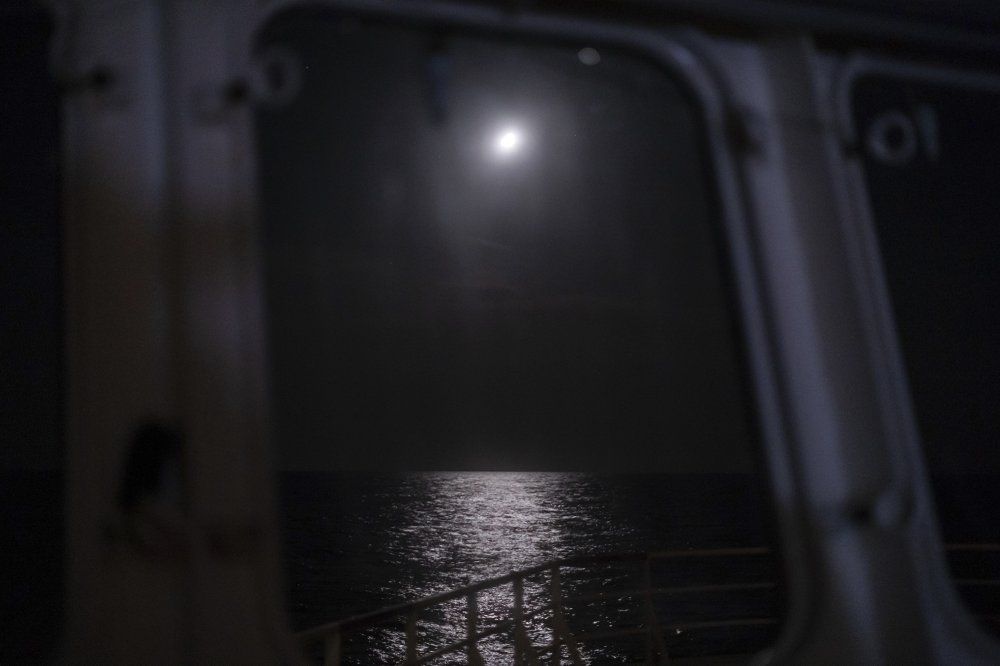 In this Sept. 7, 2019 photo, moonlight reflects from the surface of Mediterranean Sea off the coast of Libya. Husni Bey, a prominent Libyan businessman, said the idea of Europe sending aid money to Libya, a once-wealthy country suffering from corruption, was ill-conceived from the beginning. "Europe wants to buy those who can stop smuggling with all of these programs,” Bey said. “They would be much better off blacklisting the names of those involved in human trafficking, fuel and drug smuggling and charging them with crimes, instead of giving them money.” Image by Renata Brito/ AP Photo. Libya, 2019.