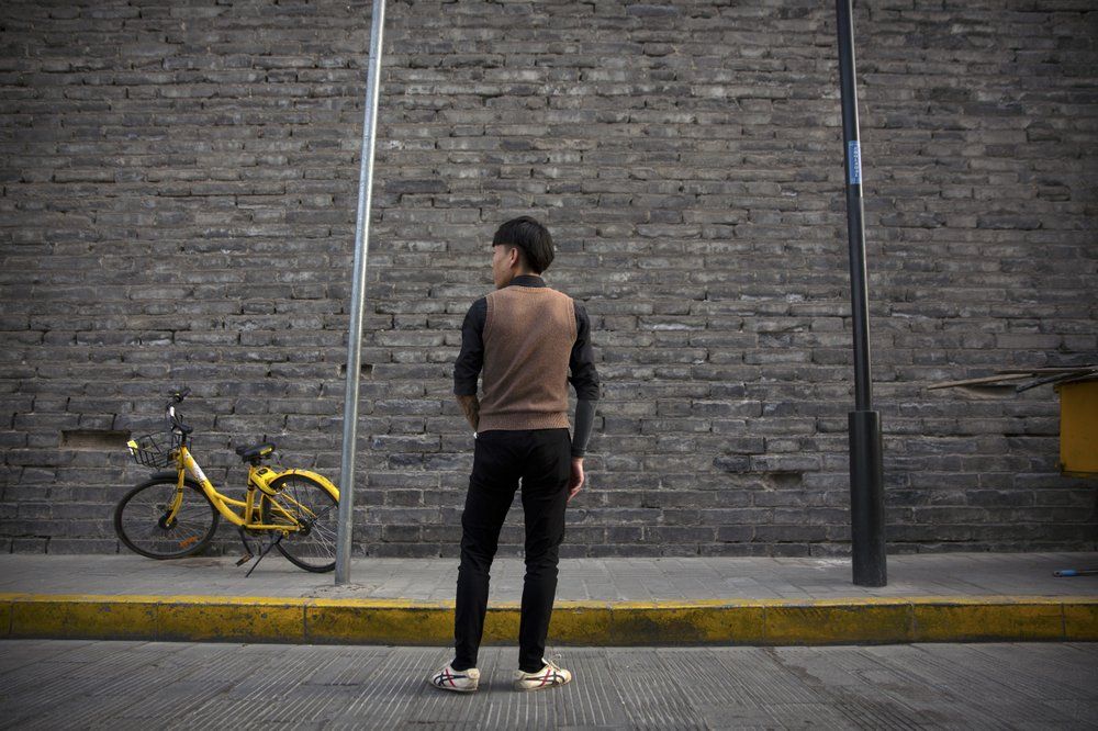 In this March 28, 2019, photo, Tylox user Yin Hao, who also goes by Yin Qiang, pauses while walking along a street near the old city walls in Xi'an, northwestern China's Shaanxi Province. Officially, pain pill abuse is an American problem, not a Chinese one. But people in China have fallen into opioid abuse the same way many Americans did, through a doctor's prescription. And despite China's strict regulations, online trafficking networks, which facilitated the spread of opioids in the U.S., also exist in China. Image by Mark Schiefelbein/ AP Photo. China, 2019.