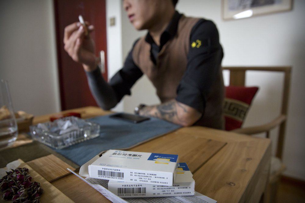 In this March 28, 2019, photo, Yin Hao, who also goes by Yin Qiang, talks about his addiction while sitting near boxes of Tylox pills he earlier purchased illicitly in a tea house in Xi'an, northwestern China's Shaanxi Province. Officially, pain pill addiction is an American problem, not a Chinese one. But people in China have fallen into opioid addiction the same way many Americans did, through a doctor's prescription. And despite China's strict regulations, online trafficking networks, which facilitated the spread of opioids in the U.S., also exist in China. Image by Mark Schiefelbein/ AP Photo. China, 2019.