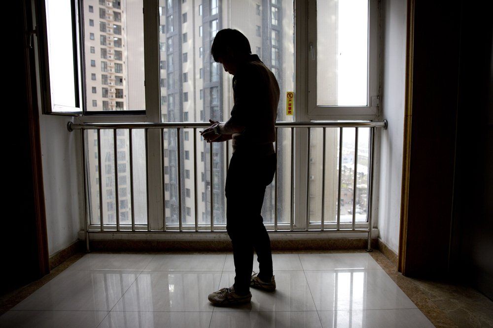 In this March 28, 2019, photo, Yin Hao, who also goes by Yin Qiang, checks his phone while standing in an elevator lobby in Xi'an, northwestern China's Shaanxi Province. Officially, pain pill abuse is an American problem, not a Chinese one. But people in China have fallen into opioid abuse the same way many Americans did, through a doctor's prescription. And despite China's strict regulations, online trafficking networks, which facilitated the spread of opioids in the U.S., also exist in China. Image by Mark Schiefelbein/ AP Photo. China, 2019.