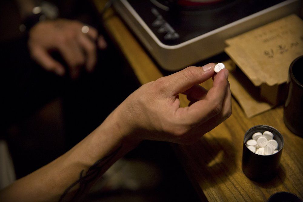 In this March 27, 2019, photo, Yin Hao, who also goes by Yin Qiang, holds a Tylox pill while sitting in a restaurant in Xi'an, in northwestern China's Shaanxi Province. Officially, pain pill addiction is an American problem, not a Chinese one. But people in China have fallen into opioid abuse the same way many Americans did, through a doctor's prescription. And despite China's strict regulations, online trafficking networks, which facilitated the spread of opioids in the U.S., also exist in China. Image by Mark Schiefelbein/ AP Photo. China, 2019.