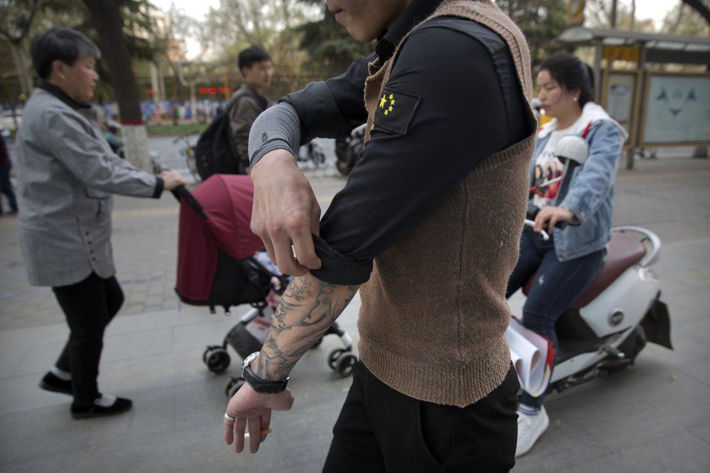 In this March 28, 2019, photo, Yin Hao, who also goes by Yin Qiang, rolls up his sleeve while walking along a street in Xi'an, northwestern China's Shaanxi Province. Officially, pain pill abuse is an American problem, not a Chinese one. But people in China have fallen into opioid abuse the same way many Americans did, through a doctor's prescription. And despite China's strict regulations, online trafficking networks, which facilitated the spread of opioids in the U.S., also exist in China. Image by Mark Schiefelbein/ AP Photo. China, 2019.